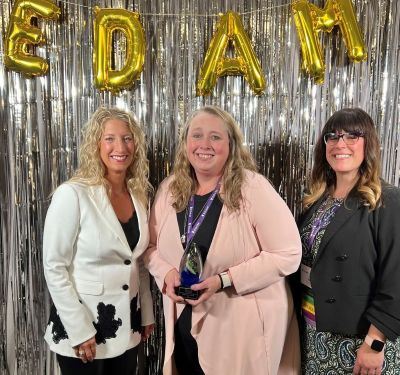 Gold EDAM Balloon Letters, woman on left in white blazer black pants, woman middle in pink blazer bl