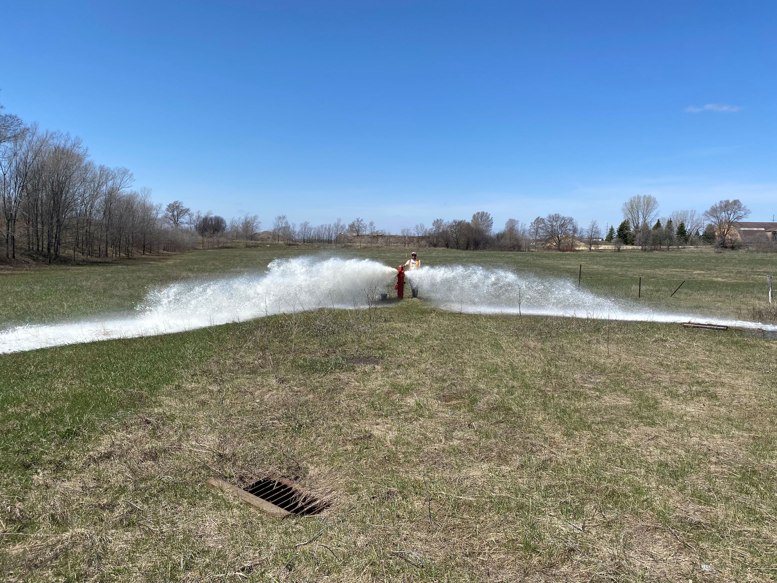 Fire hydrant with water spraying from two opposite sides onto grass